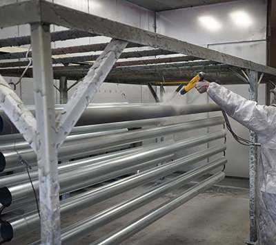 A worker applying a protective finish or premium powder coating to metal pipes
