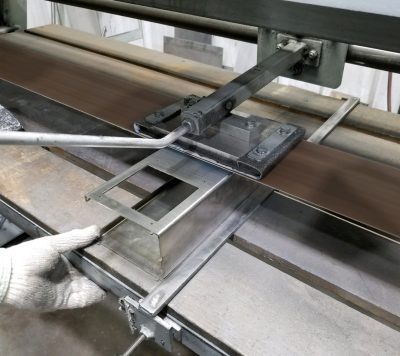 A worker using a sheet metal bending machine (such as a press brake or manual folding machine) to form precise angles in a piece of sheet metal