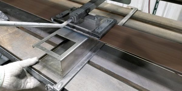 A worker using a sheet metal bending machine (such as a press brake or manual folding machine) to form precise angles in a piece of sheet metal